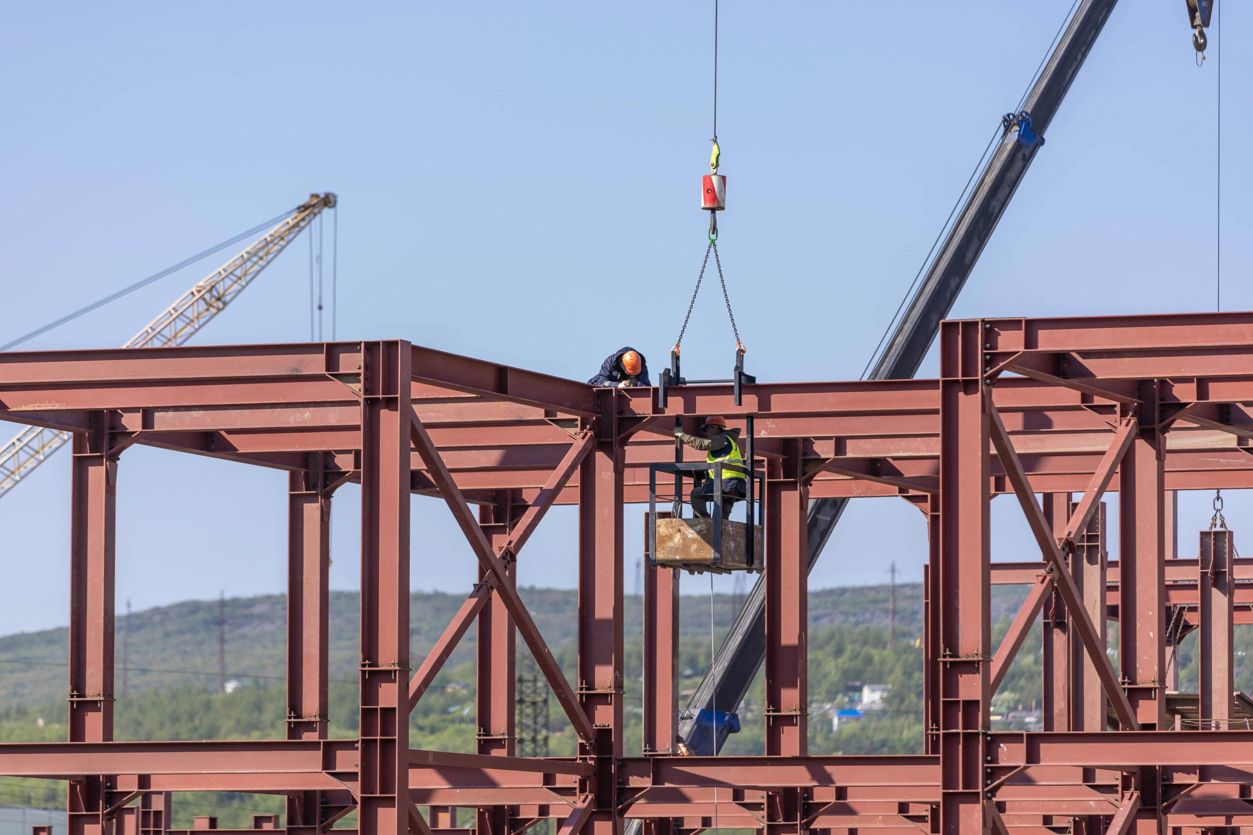 Construction workers assembling steel frame structure with cranes in daylight outdoors.